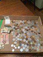 Wide shot showing the collection of various coins spread out in a cardboard box along with Canadian bills.