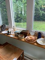 Wide view of all items arranged on window ledge showing a mix of pottery, glass, wood, and metal pieces.