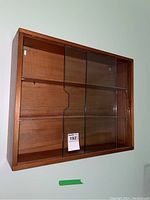 Front view of teak display case mounted on wall showing full unit with sliding glass doors.