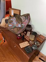 Various art and decor items on wooden surface, featuring stamped Asian god figure artwork, pottery pieces, wooden boxes, carved elephants, and stones.
