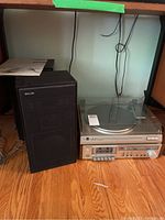 Photo showing black Philips speaker and Dual CS 514 turntable with dusty clear cover, on hardwood floor under shelf.