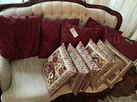 Five burgundy textured cushions and six floral patterned fringed cushions arranged on a cream tufted sofa.