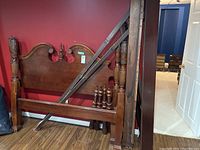 Overview of dismantled wooden bed frame components leaning against red wall: headboard, footboard, side rails, posts