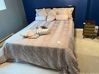 Queen bed dressed with beige patterned bedspread, pillow shams, and accent pillows, showing overall set condition and appearance