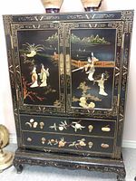 Front view of black lacquered Japanese cabinet with two drawers and decorative doors showing painted figures, landscape, and damaged left door.