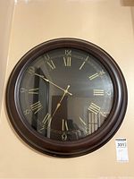 Front view of large wall clock with dark wooden frame, black face and gold Roman numerals