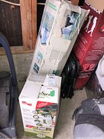 Boxed 10x10 gazebo and boxed Graco SureSpray sprayer stacked in storage area