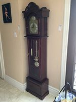 Tall grandmother clock in corner, showing full height and details of wood case, clock face, pendulum, and weight