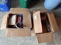 Two cardboard boxes containing a mixture of Hebrew books and binders, some stacked vertically and others horizontally.