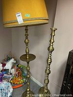 Two brass floor lamps positioned in corner, one with yellow lampshade, one missing lampshade showing brass finish and design