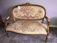Front view of loveseat showing carved giltwood frame and floral tapestry upholstery