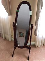 Full view of the standing mirror showing the oval mirror glass and wooden frame with supporting legs.