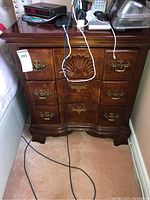 Front view of full nightstand showing shell carving, drawer layout, brass handles and scalloped base.