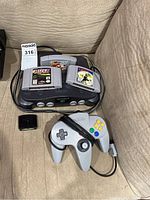 Nintendo 64 console with three game cartridges on top, one gray controller, and black jumper pak memory card visible.