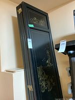 Four-panel wooden screen folded, showing black finish with gold Asian-style illustrations and brass hinges.
