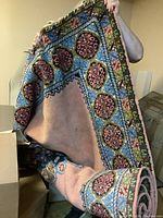 Rug held up showing the overall design, colors mostly pink center with blue and green borders with floral motifs.