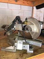 Side view of Concept brand mitre saw showing full saw body on wooden shelf in garage, with power cord and blade guard visible.