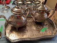 Photo showing the silver tone tea set with teapot and hot water pot on an ornate tray with detailed etched design.