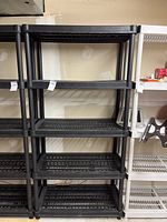 Photo showing full view of black plastic utility shelving unit with multiple tiers and slotted grid shelves.