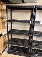 Full front view of black plastic utility shelves with five grated shelves and round legs.