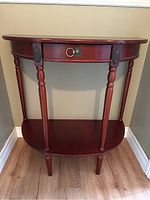 Front view of the half-moon table showing small drawer, carved legs, and lower shelf.