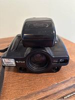 Front view of the black Fuji Auto Focus 35mm camera with lens visible and accessory flash attached on top.