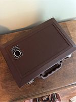 Closed brown case with Olds logo sticker on top, placed on wooden table.