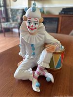 Front view of seated clown figurine showing painted face, white ruffled costume, and details on drum.