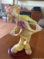 Front left angled view of clown figurine showing detailed facial features, colorful outfit, and wooden base.