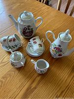 Porcelain coffee and tea set arranged on wooden table showing all components including pots, cups, saucers, sugar bowl, and creamer.