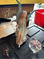 Photo showing front side of the fairy figurine sitting with blue wings extended and crystal paperweight to the right.