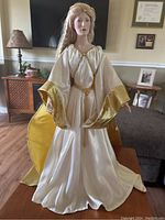 Full frontal view of the Franklin Heirloom Queen Galadriel doll standing dressed in cream satin gown with gold trim and braided belt.