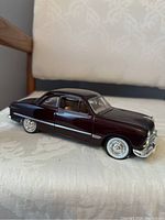Black older model car on chair with chrome details and whitewall tires
