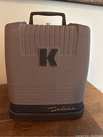 Front view of Keystone K Deluxe projector with handle, showing logo and casing.