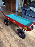 Side angled view of the red and blue painted wooden wagon with floral decoration and black wheels on wood floor.