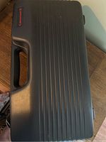 Closed black hard carrying case with handle and ridged exterior surface.