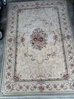 Top-down photo showing the floral pattern rug with central bouquet and decorative border in teal, burgundy, beige colors.