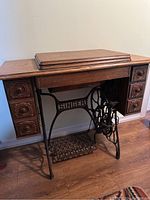 Full view of the vintage Singer treadle sewing machine set in its wooden cabinet with detailed carving and multiple drawers.