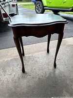 Full view of the small wooden side table showing curved edges and cabriole legs