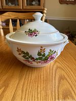 White ceramic soup tureen with lid decorated with floral pattern on a wooden table