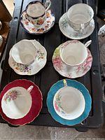 Top-down view of all six English teacups with matching saucers showing various floral designs and gold trim.