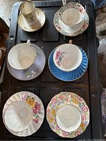 Top-down view of six teacups with matching saucers, each exhibiting unique floral patterning and gold trim.