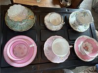 Overview photo showing all 6 teacups and saucers in various patterns and colors, placed on black background.
