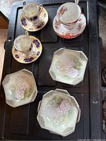 Photo showing 3 teacups with matching saucers; two have cream/dark blue floral design, one has red/pink floral design.