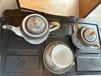 Teapot, sugar bowl, teacup, and saucer on black surface showing overall design and shape