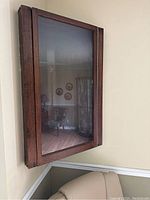 Wall mounted wooden corner cabinet showing front glass door and reflective glass surface.