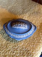 Blue Wedgwood jasperware oval covered box with white classical relief figures and foliage on lid and sides.
