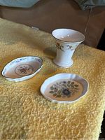 Three-piece lot of Wedgwood porcelain dishware on a yellow textured surface: pedestal cup and two small dishes with floral patterns.