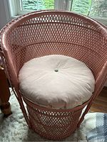 Peach wicker chair with white round cushion on seat, showing woven lattice back and base