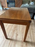 Front angle of wooden side table showing tapered legs and rectangular top surface on wood floor.